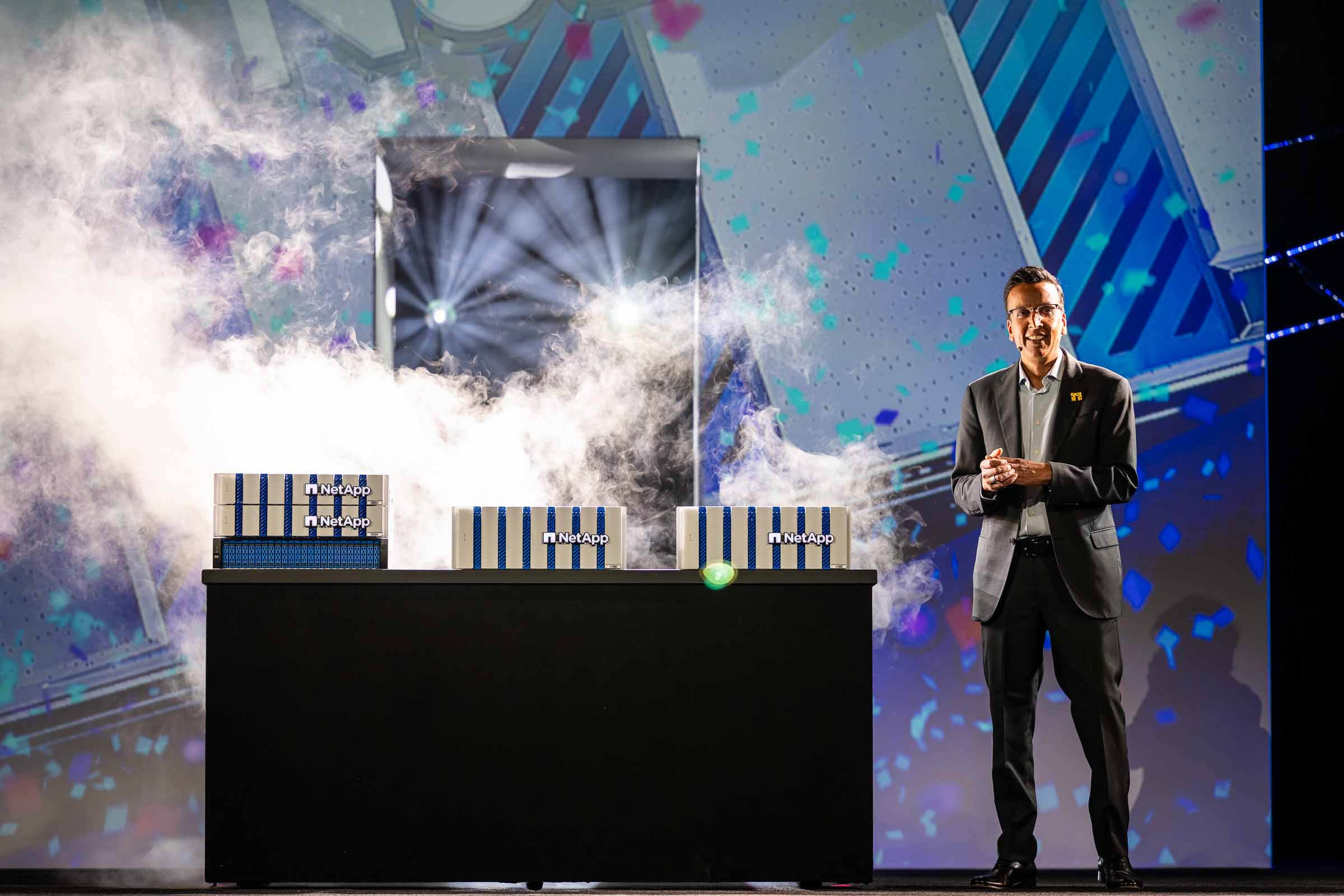 Executive presenter on stage with dramatic atmospheric effects and branded display