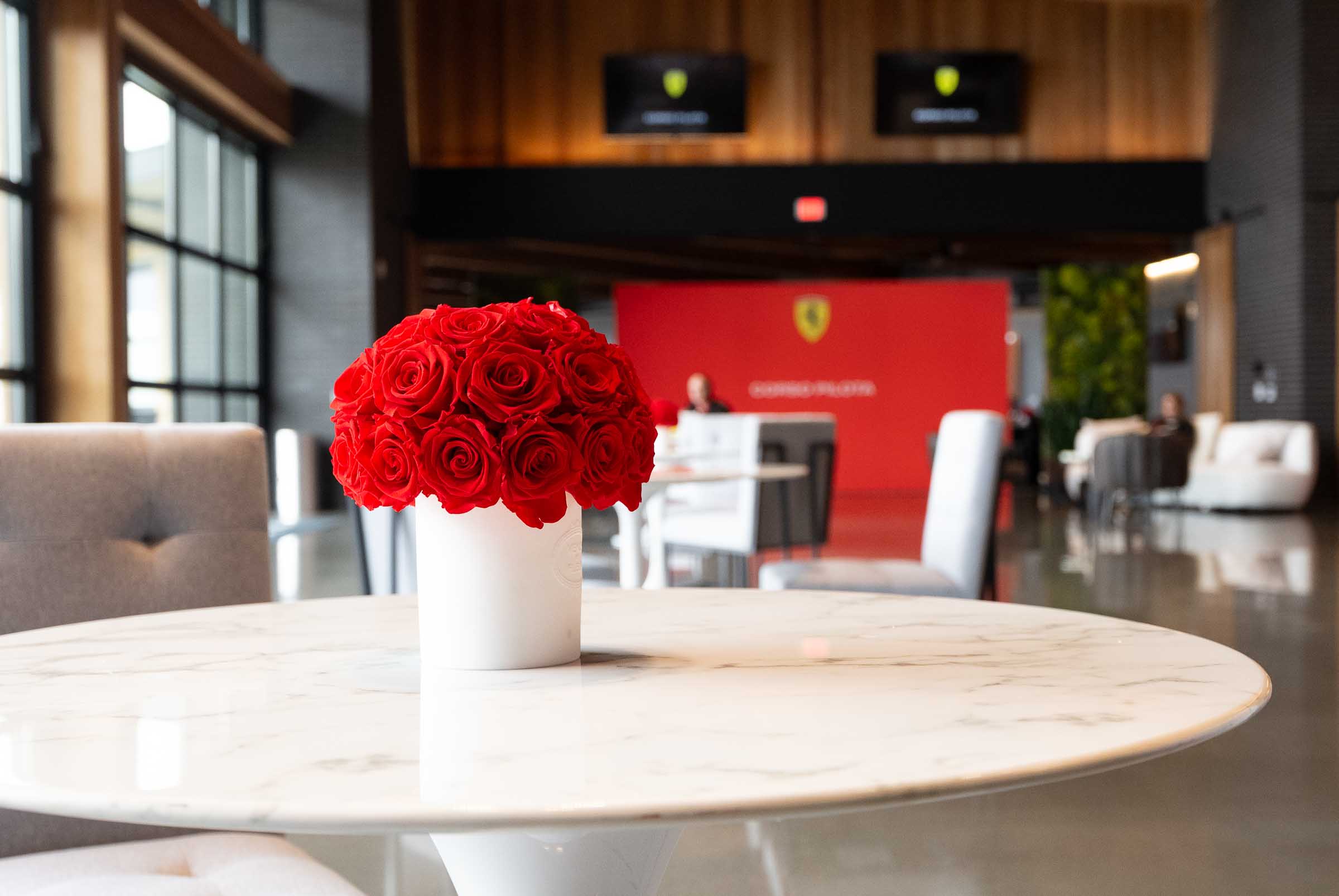 Illuminated building facade featuring lit windows displaying colorful Ferrari branding and signage in early evening