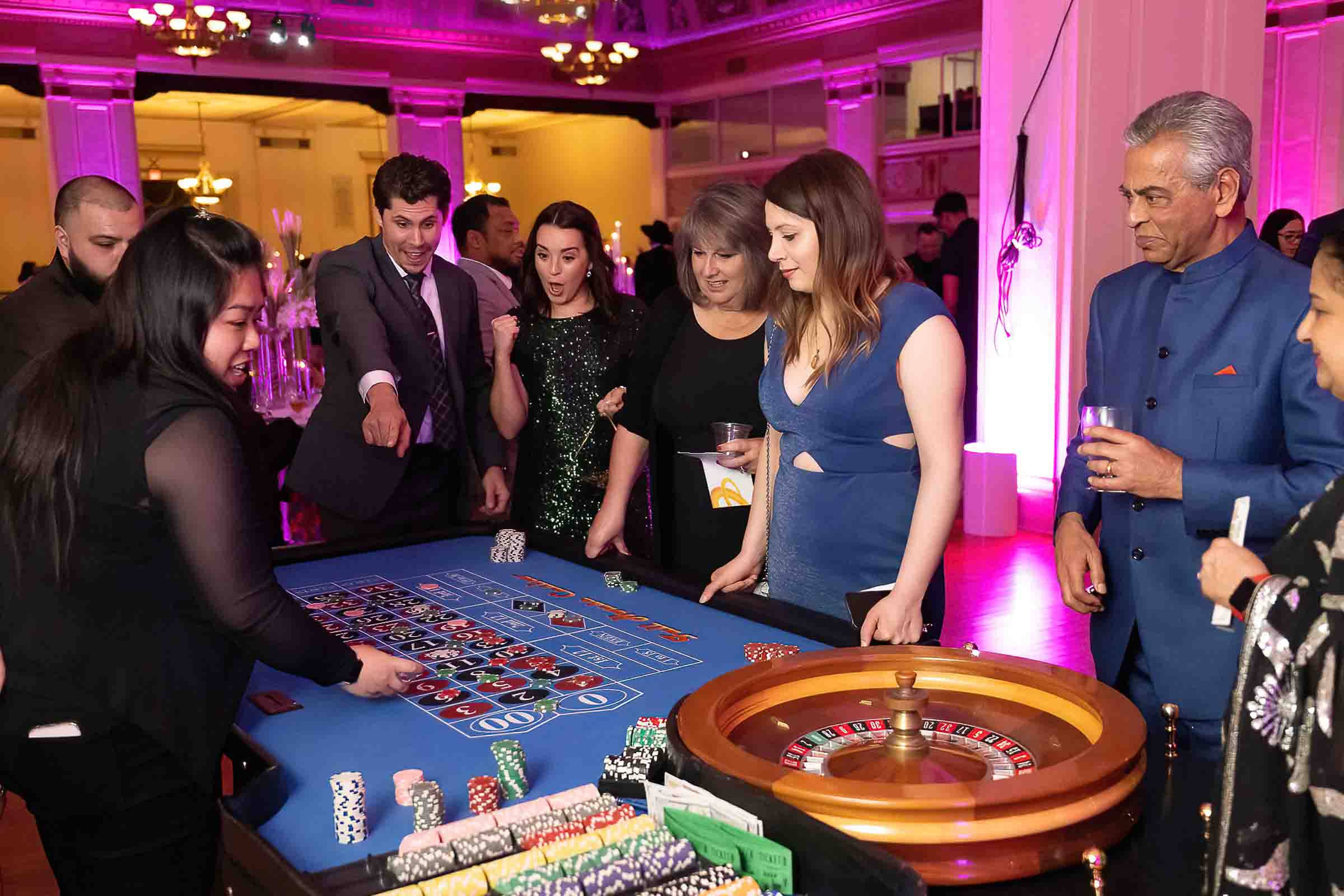 Guests gathered around casino tables at formal gala with pink uplighting