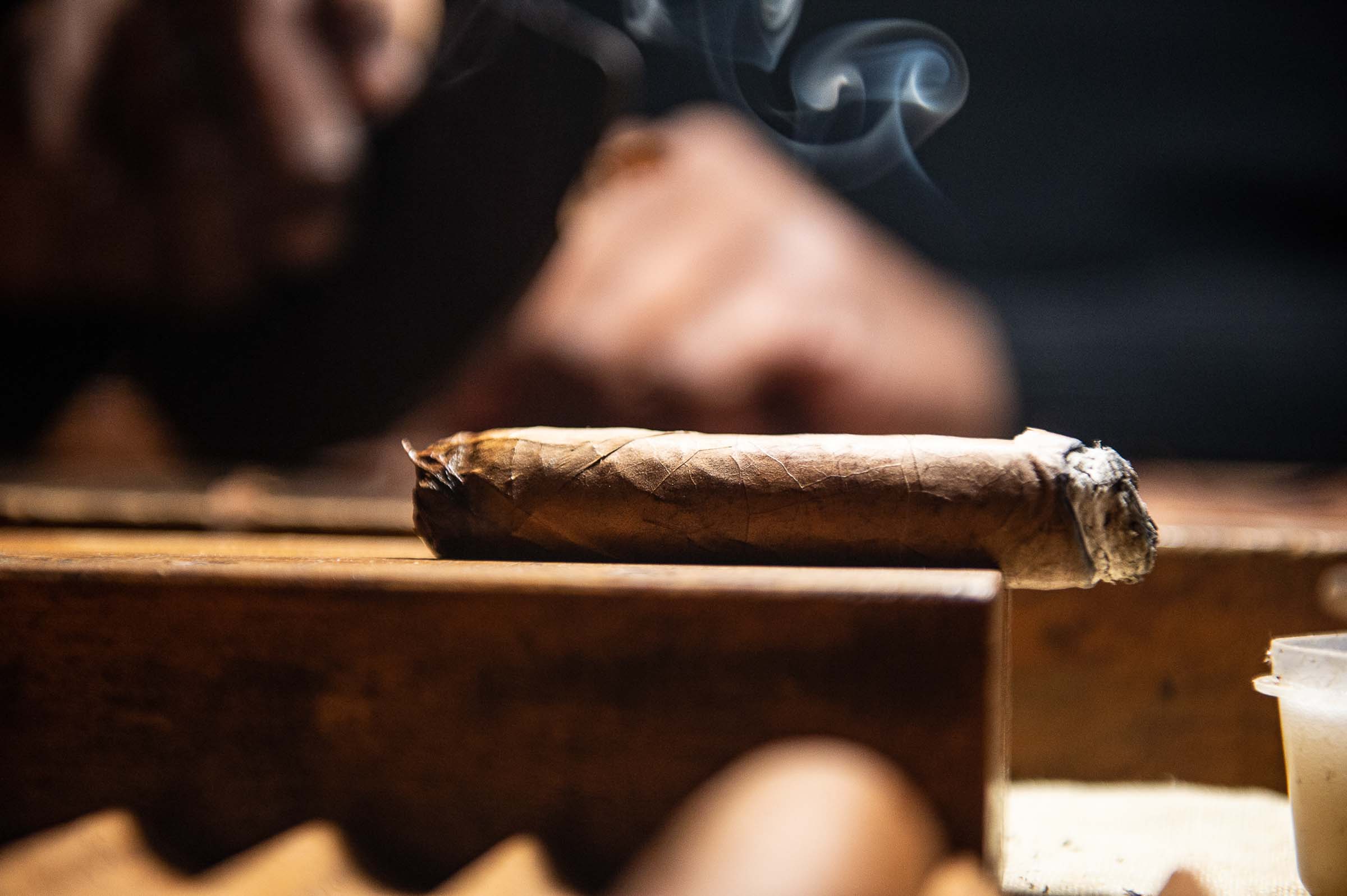 Lit cigar resting on wooden surface with wisps of smoke curling upward at upscale event lounge