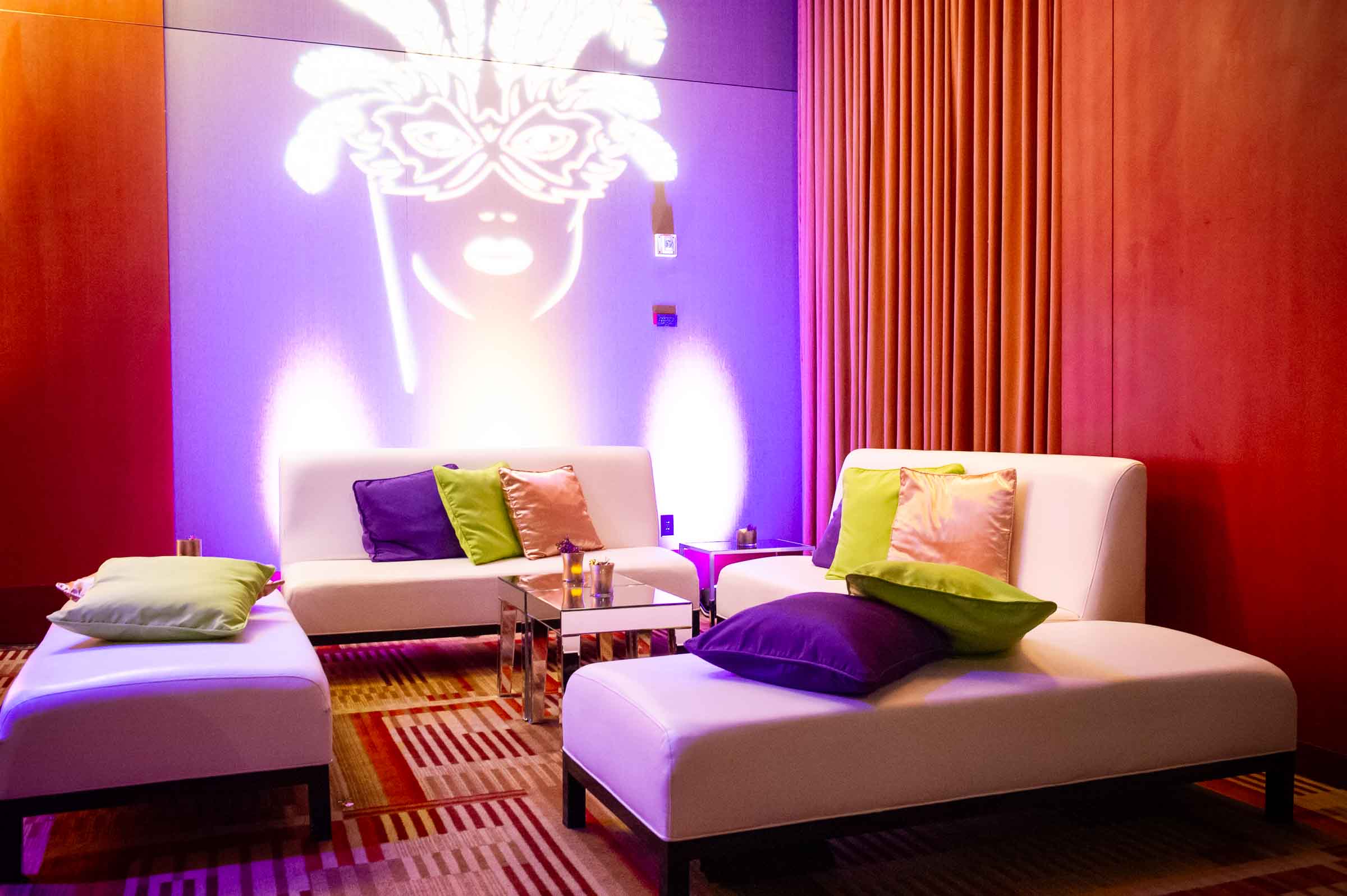 Stylized illuminated masked face projection above modern lounge seating with colorful pillows