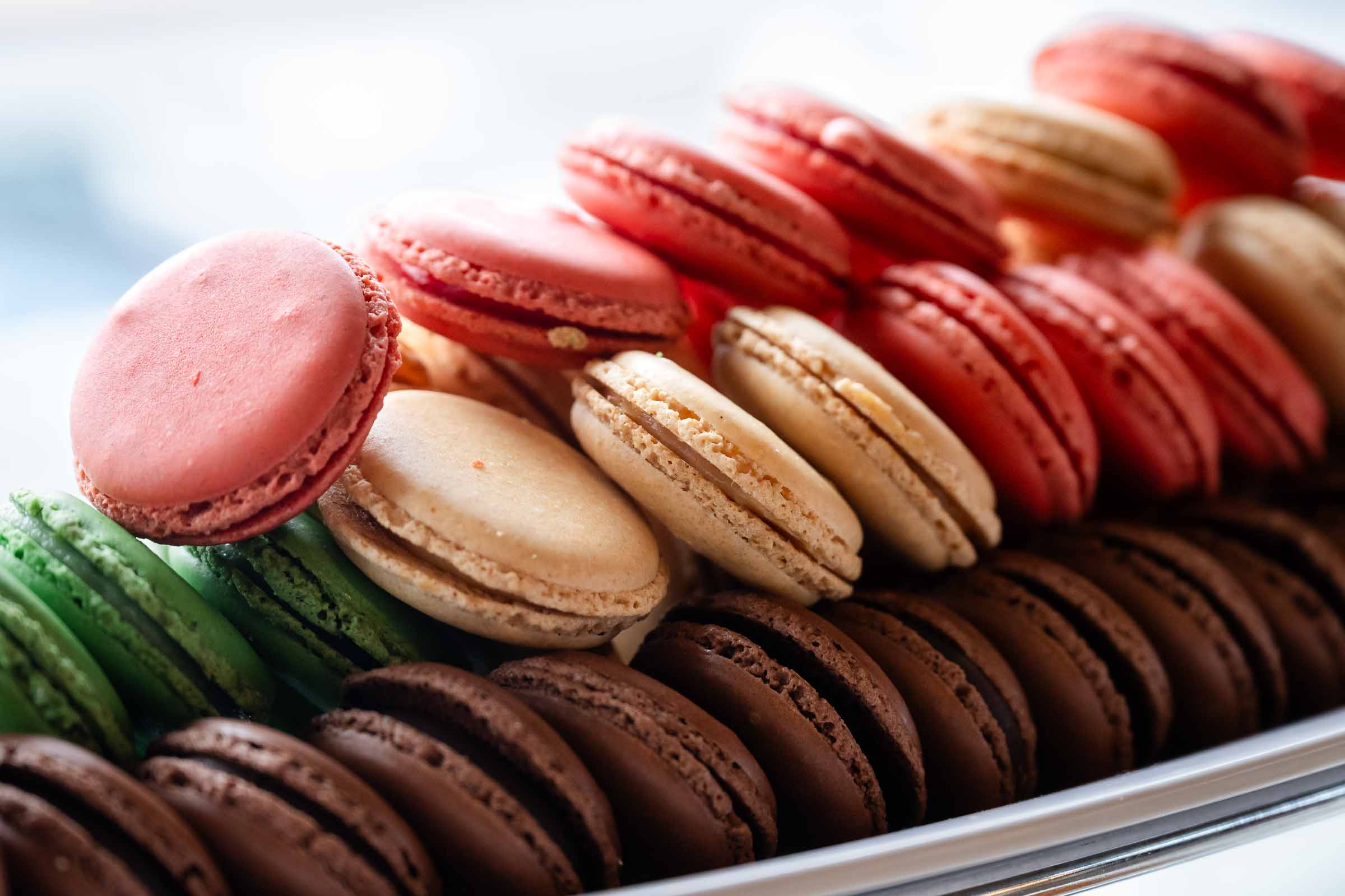 Rows of assorted French macarons in pink, green, cream, chocolate, and red arranged on serving tray