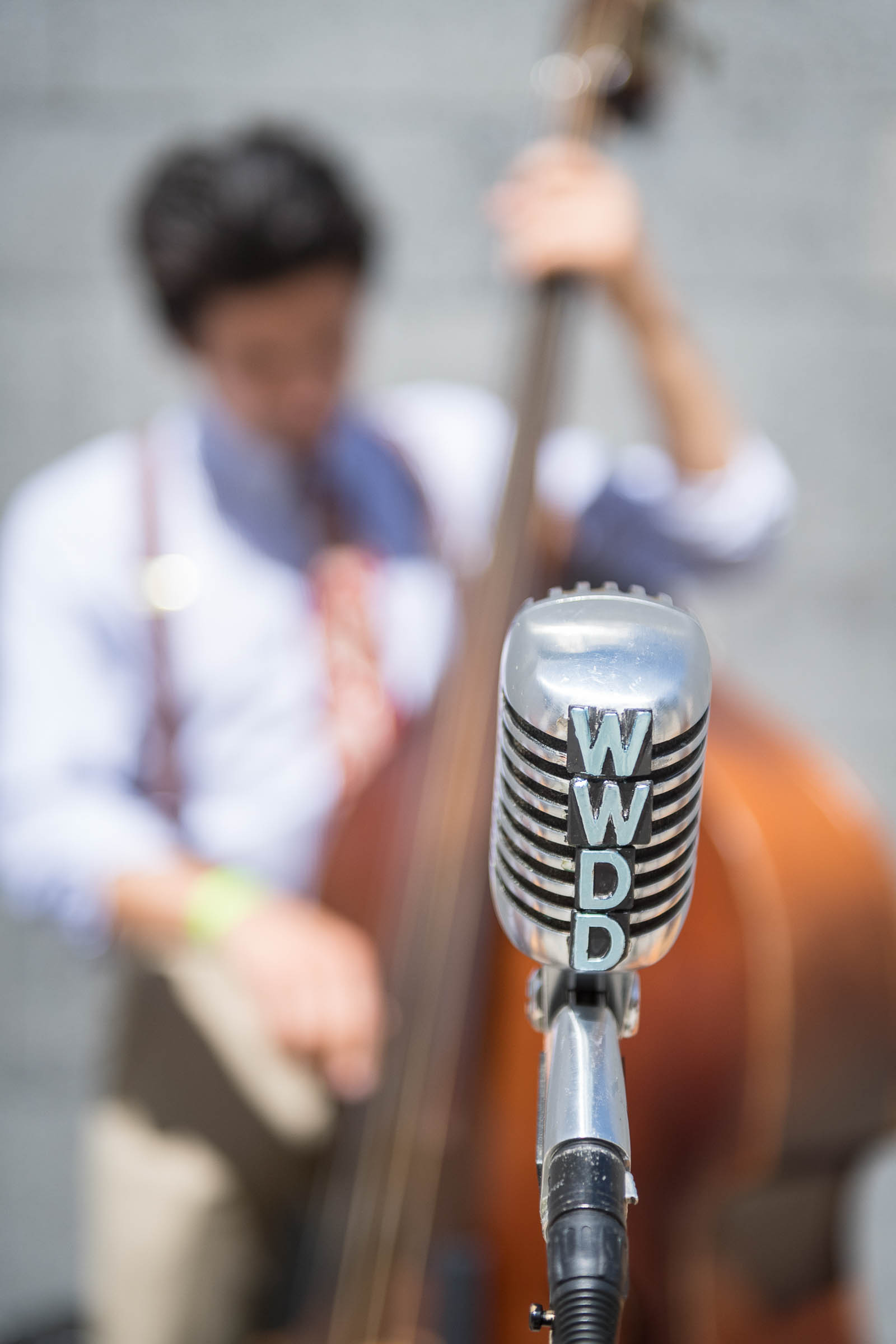 Vintage chrome microphone in sharp focus with blurred upright bass musician in background